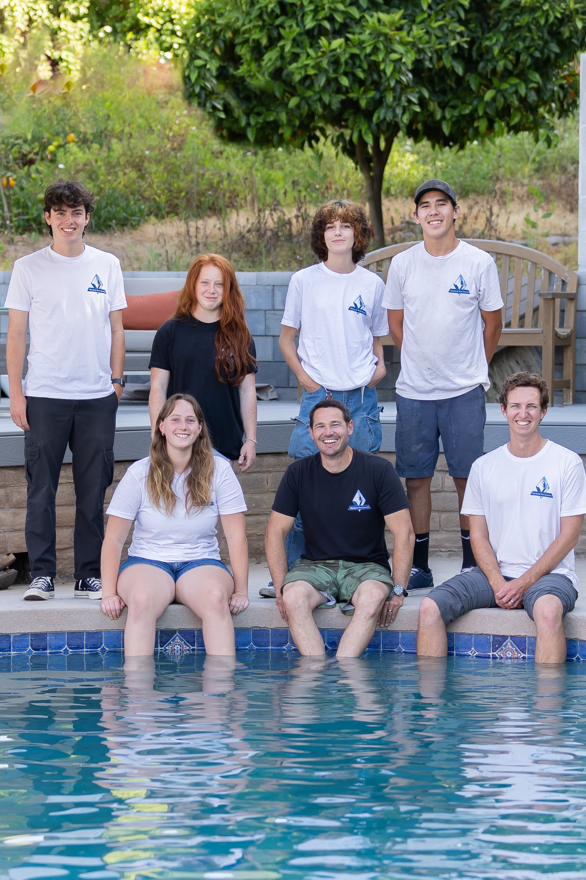 Murdock Pool Service crew sitting by a pool with feet in the water