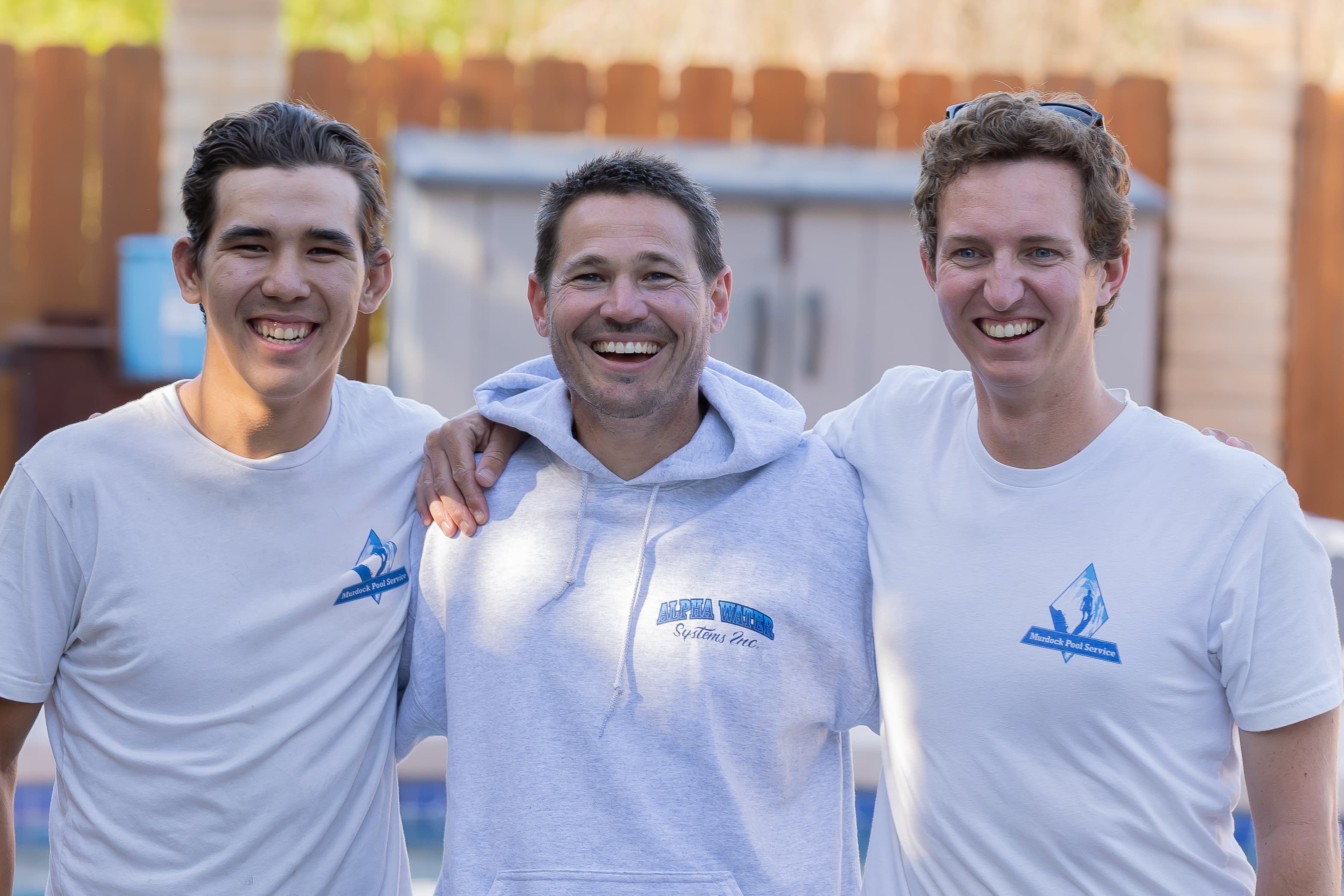 Brett Murdock with two team members smiling in front of pool equipment