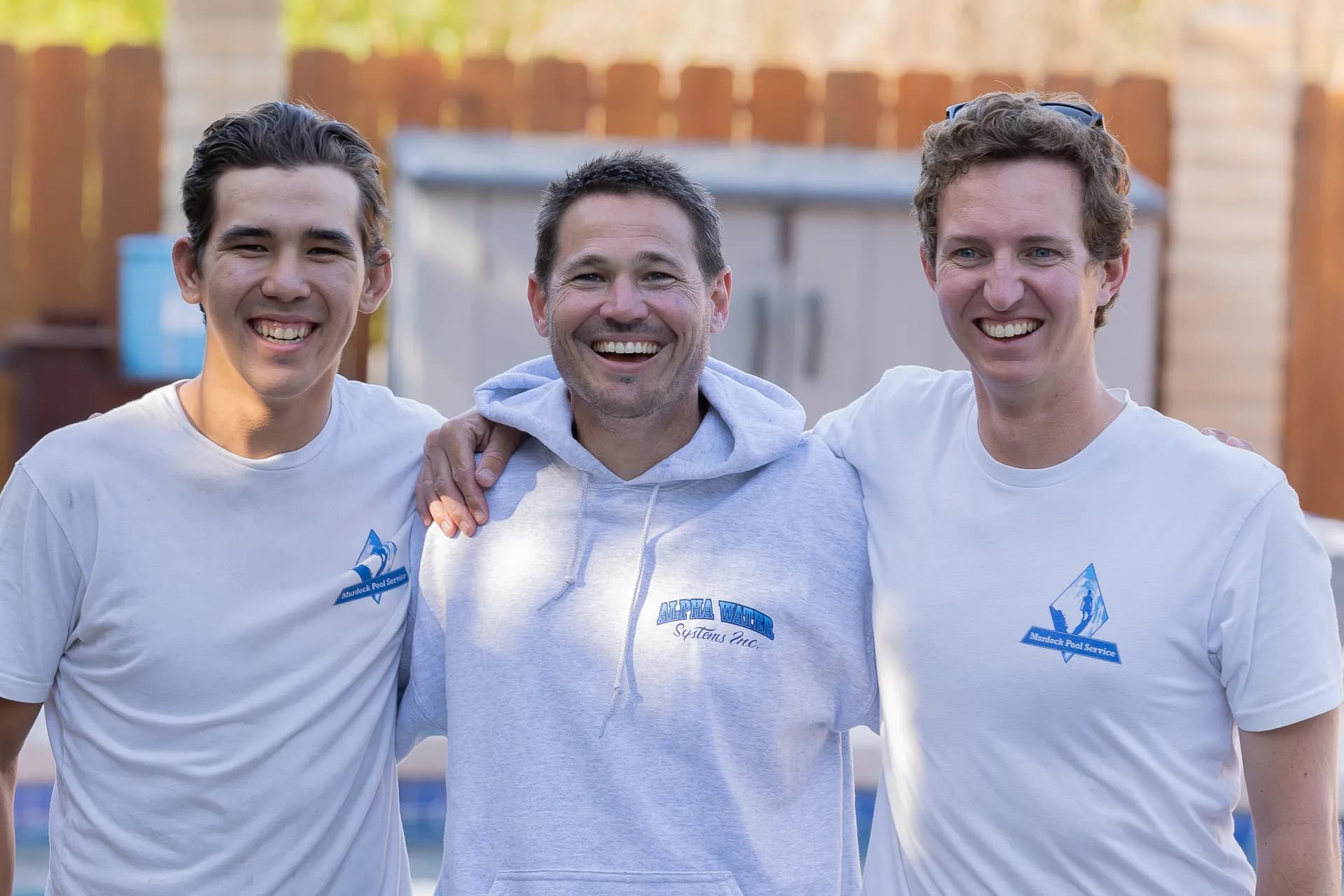 Brett Murdock with two team members smiling in front of pool equipment