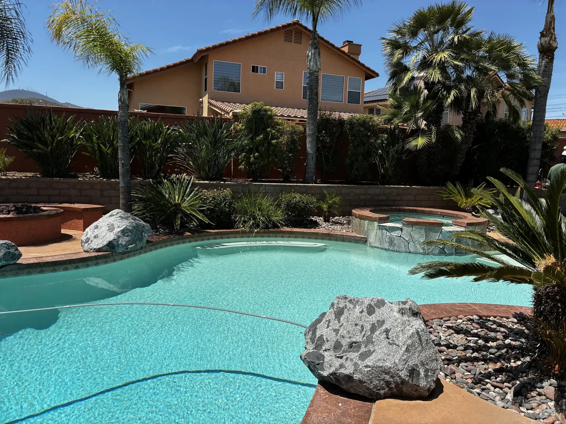 Customer pool and attached spa with boulder accents in front of a Spanish-tile San Diego home