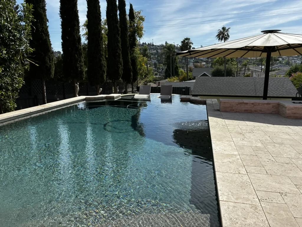 Infinity-edge customer pool framed by cypress trees with a hilltop view, maintained by Murdock Pool Service