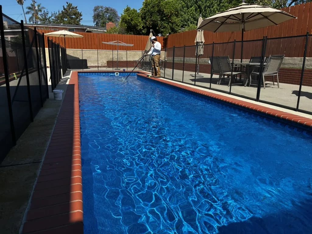 Murdock Pool Service technician skimming the surface of a long rectangular residential pool in El Cajon