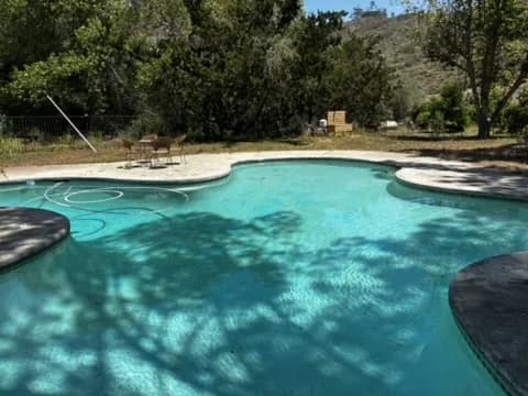 Wide view of a Murdock Pool Service technician working a residential pool in El Cajon hill country under dappled shade