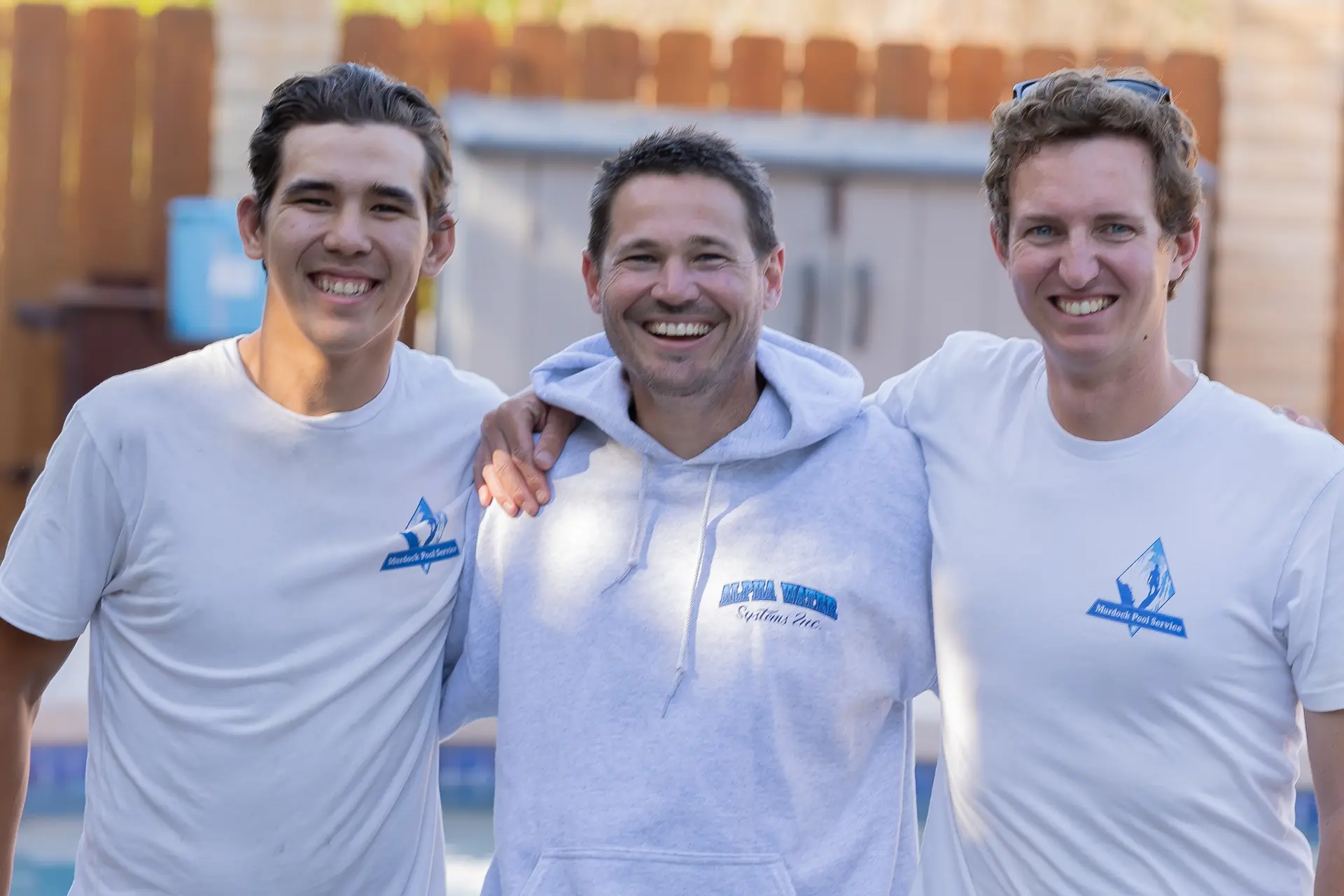 Brett Murdock with two team members, arms around each other, smiling poolside