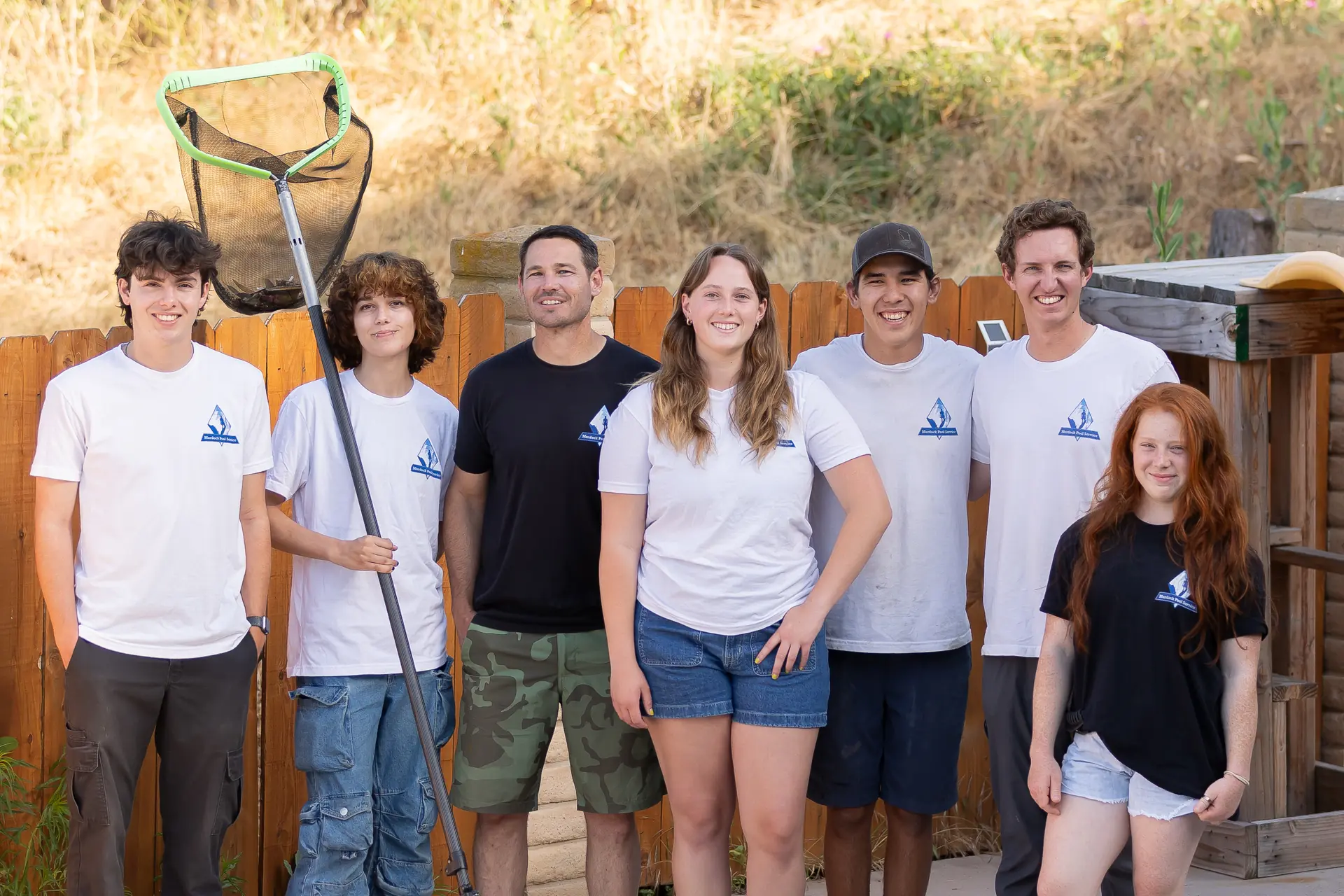 The Murdock Pool Service crew gathered with skimmer and branded shirts at a San Diego customer pool