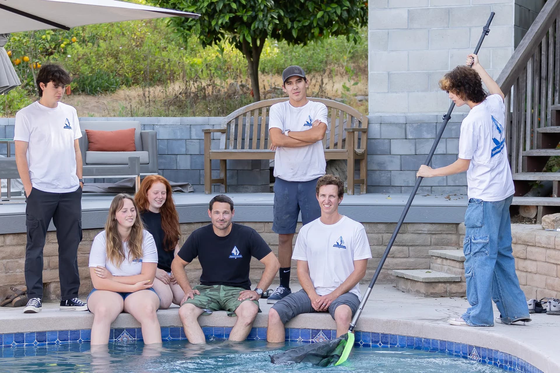 Murdock Pool Service team gathered with pool net, ready to balance pool chemistry